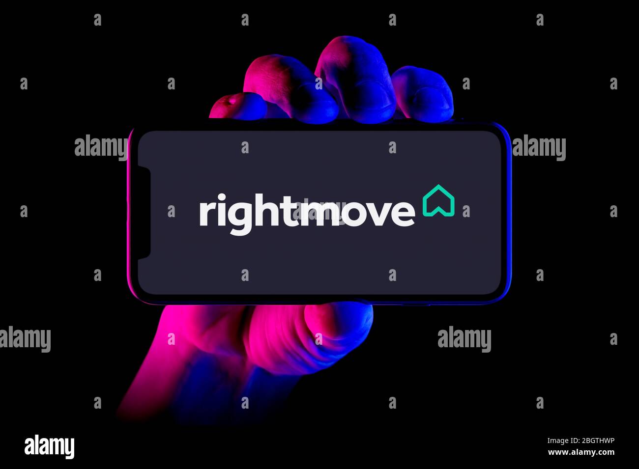 A smartphone displaying the Rightmove logo is held by a hand shot on a black background (editorial use only). Stock Photo