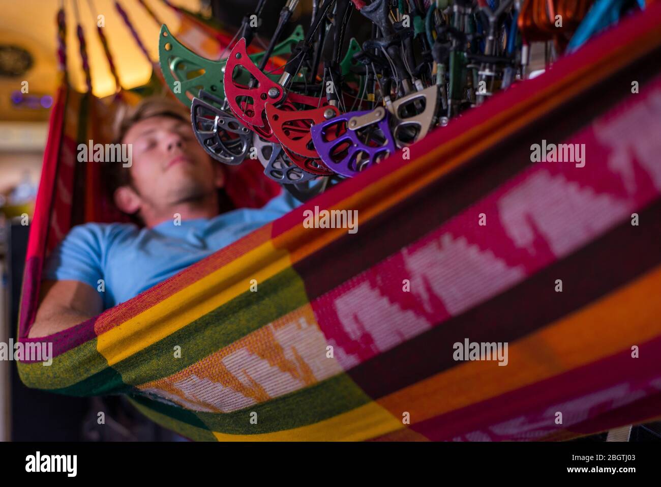 Man sleeping in hammock inside bus under lots of climbing gear hanging Stock Photo