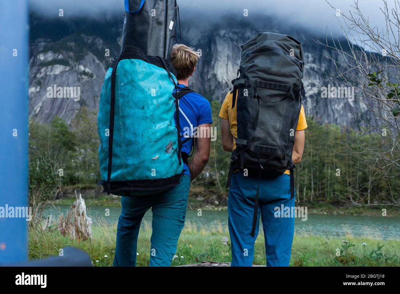 Two people with big backpack standing in front of mountain and river Stock Photo