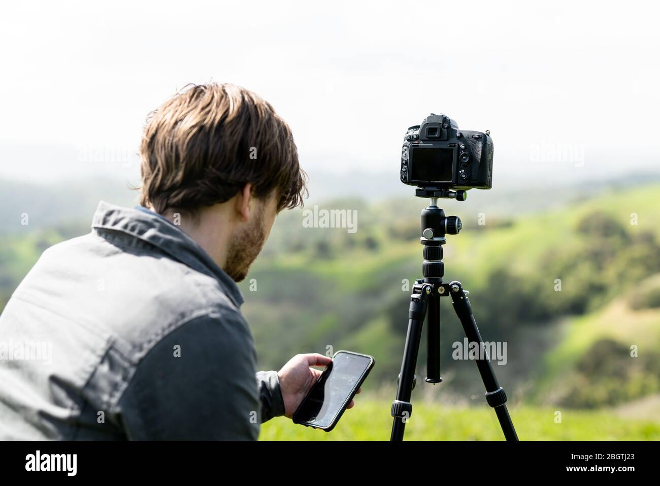 Person using smartphone app to control camera on tripod outdoors Stock Photo