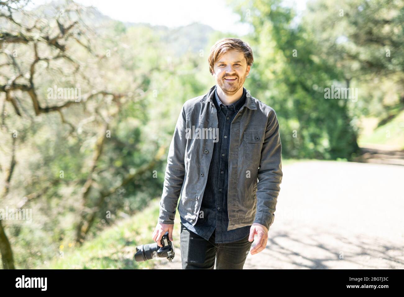 Portrait of young person smiling while walking on trail holding camera Stock Photo