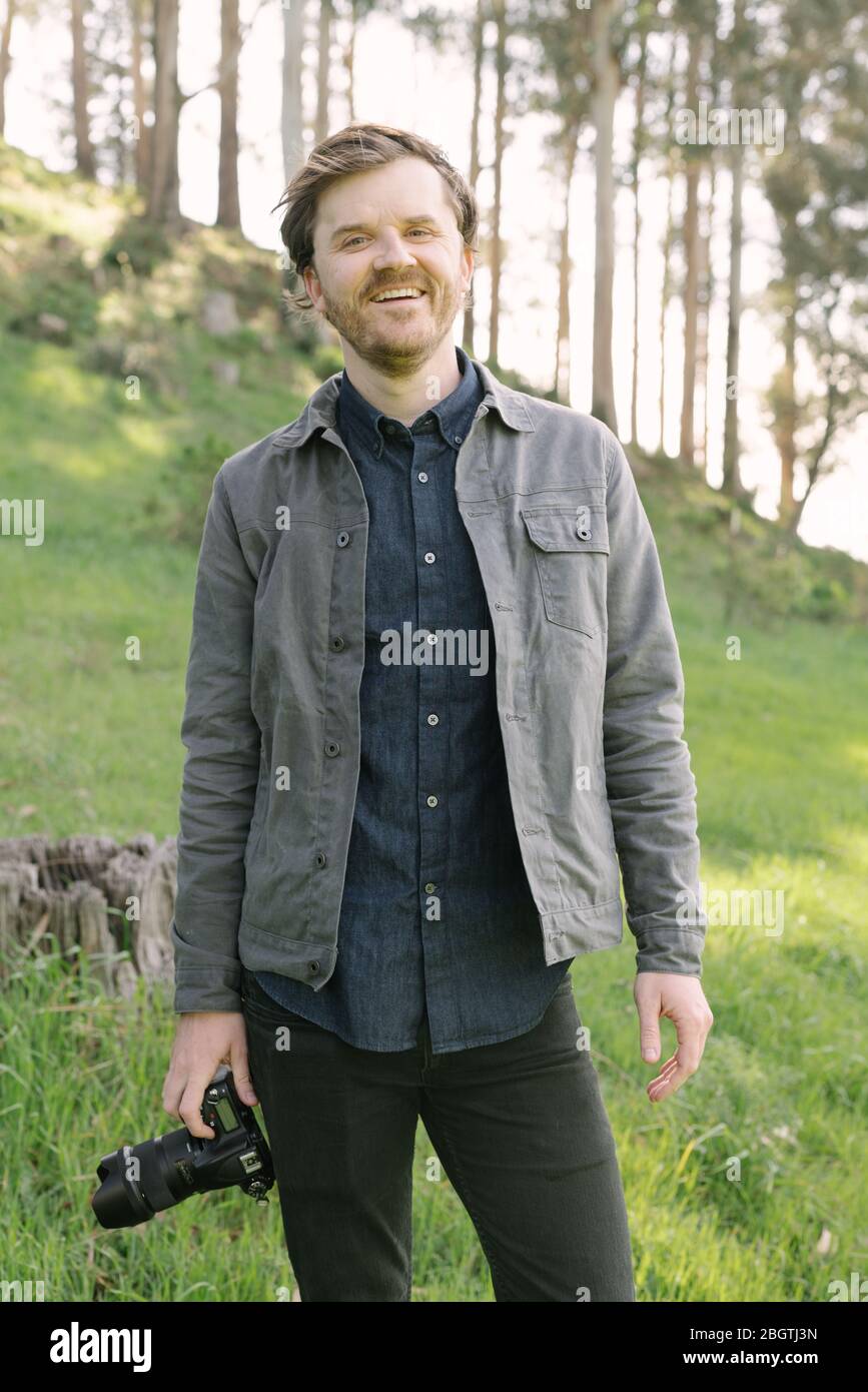 Man smiling outdoors looking into camera in casual dress with camera Stock Photo