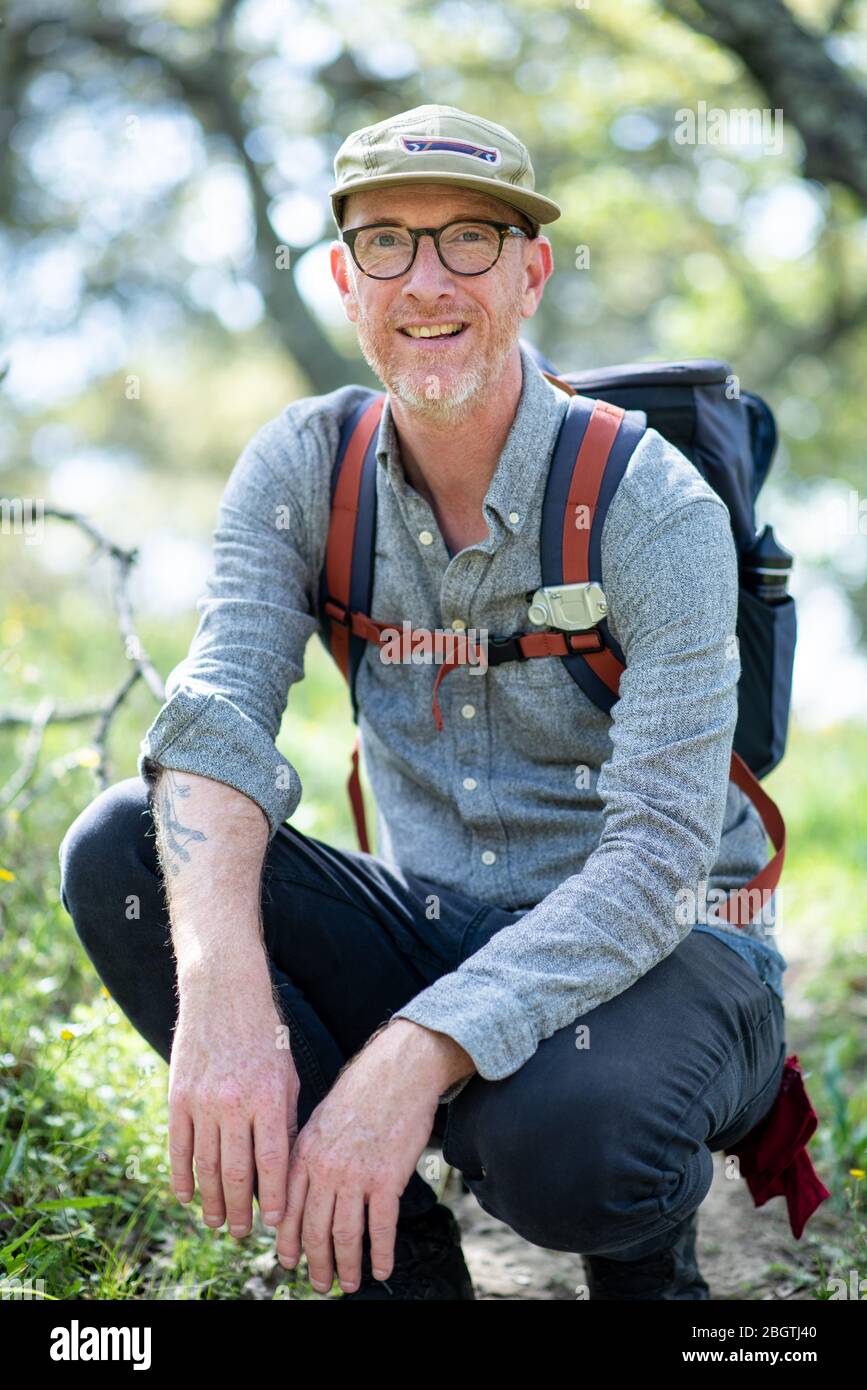Portrait of backpacker kneeling on trail and smiling in California Stock Photo
