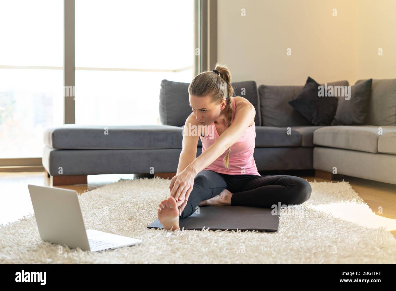 Online sport fitness yoga training. woman doing exercises on yoga mat opposite laptop online master class. training at home. Stock Photo