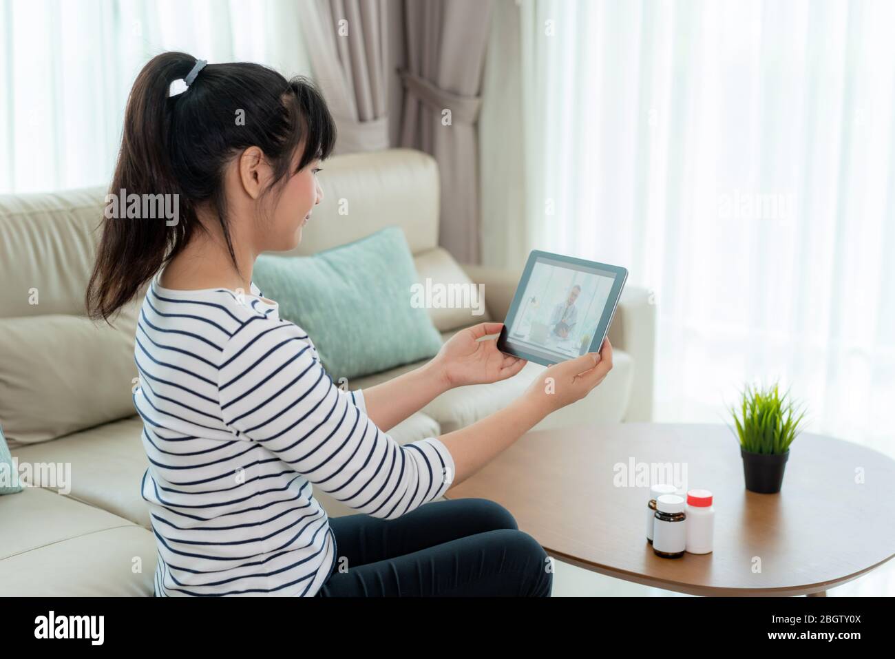 Back view of woman making video call with her doctor while staying at home. Close up of patient in video conferencing with general practitioner on dig Stock Photo