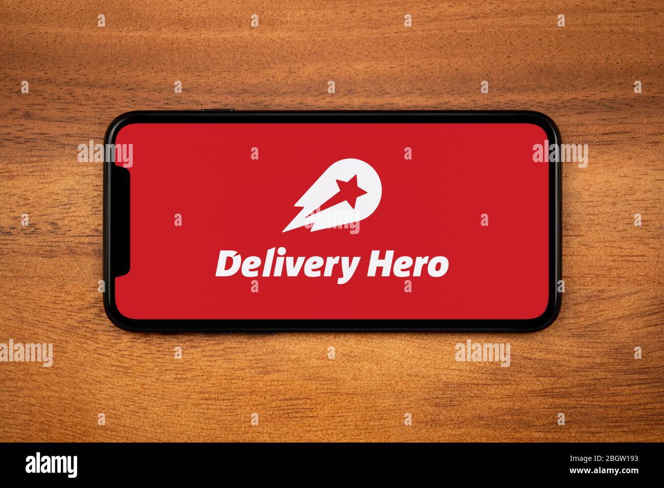 A smartphone showing the Delivery Hero logo rests on a plain wooden table (Editorial use only). Stock Photo