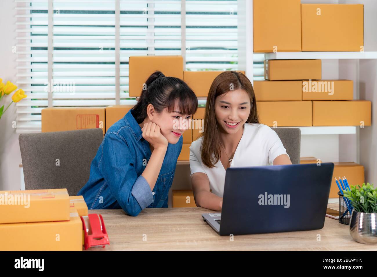 Two Asian teenager owner business woman work from home on the table for online shopping, checking order for delivery mail shipping with office equipme Stock Photo