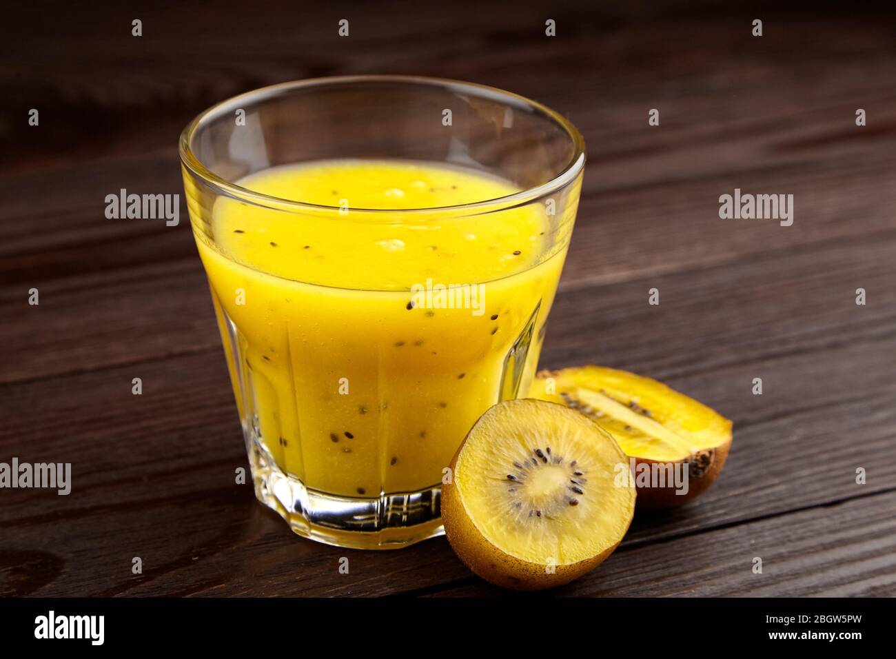 Kiwi gold fruit juice in transparent glass on wooden table. Half of yellow kiwi. Fresh kiwi smoothie. Healthy food and drink Stock Photo