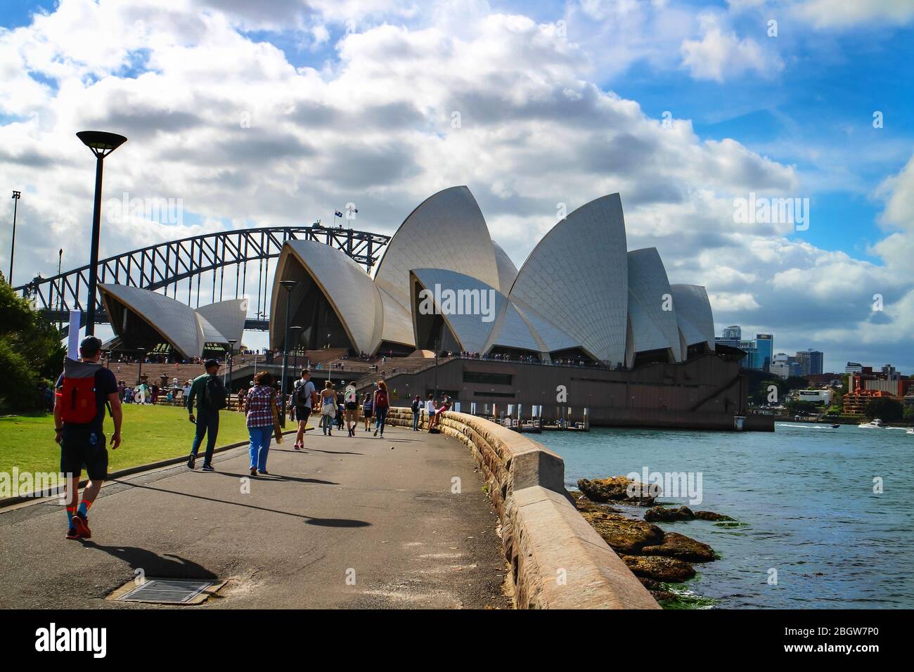 Tourism in Sydney with visitors walking along the waterfront of Sydney Harbor with a view of iconic Sydney Opera House and Harbour Bridge. Stock Photo