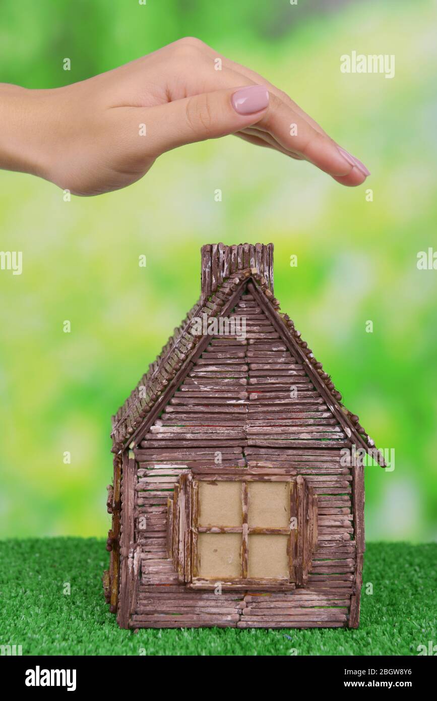 Small house with woman hand on grass on bright background Stock Photo ...