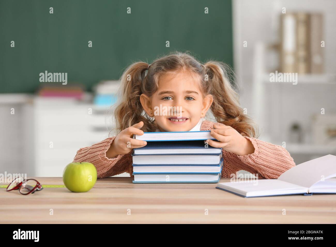 Cute little schoolgirl with books at desk in classroom Stock Photo - Alamy