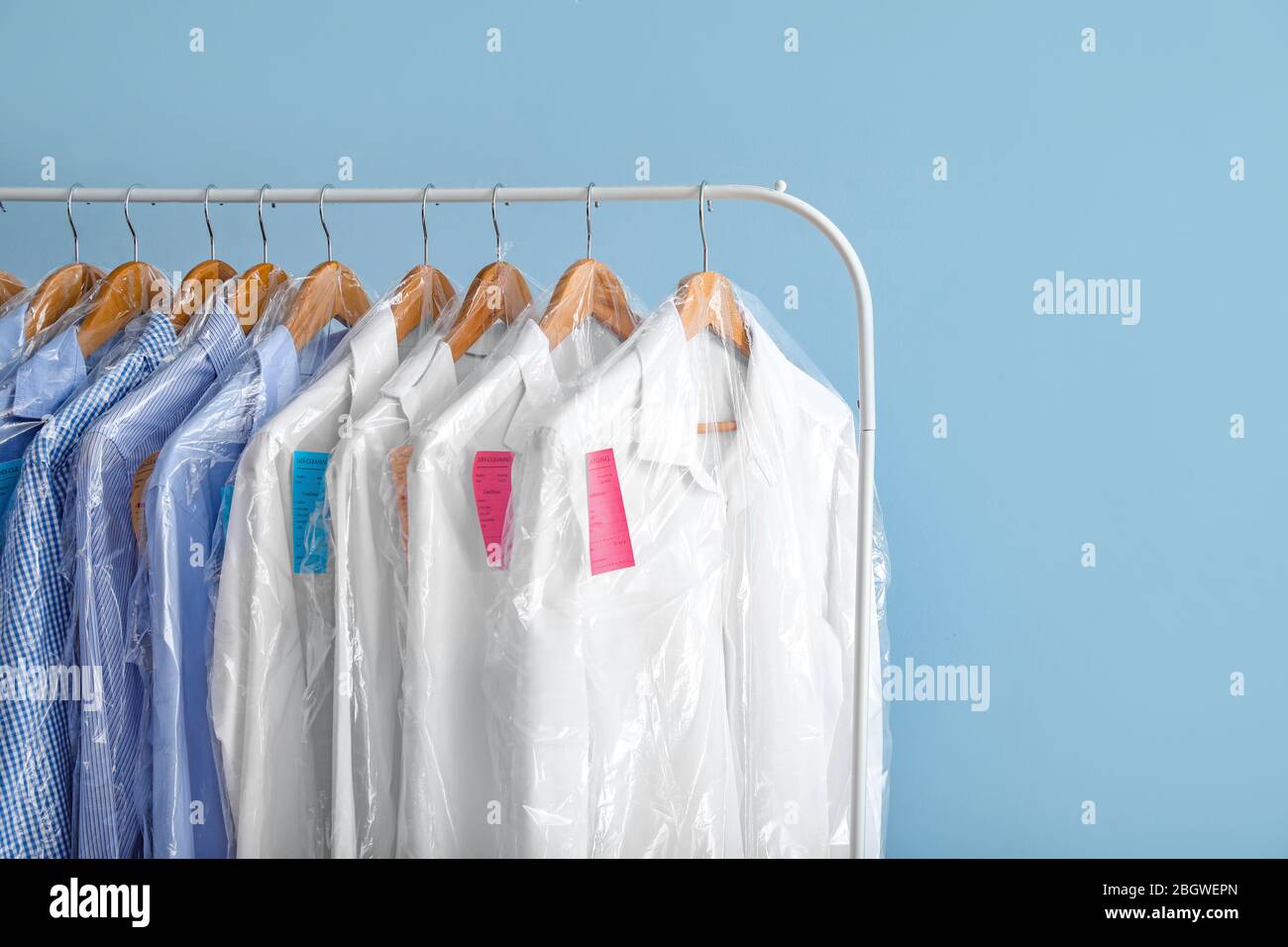 Rack with clothes after dry-cleaning on color background Stock Photo - Alamy