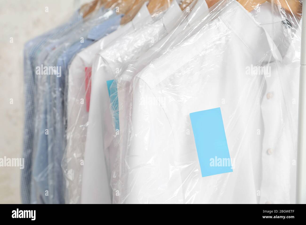 Rack with clothes after dry-cleaning on light background, closeup Stock