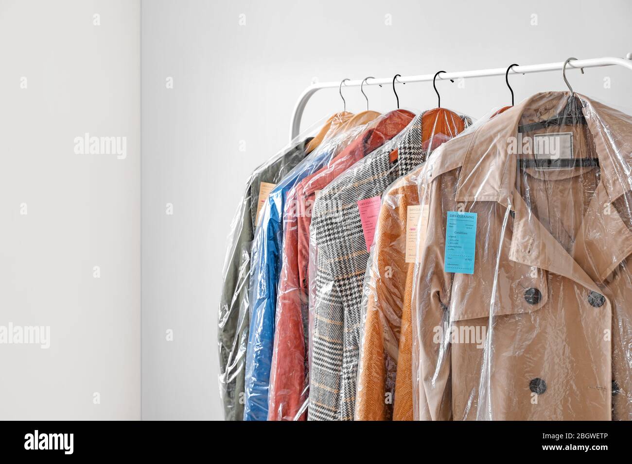 Rack with clothes after dry-cleaning on light background Stock Photo - Alamy