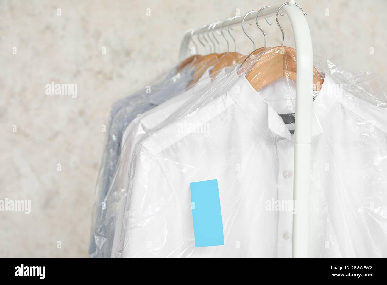 Rack with clothes after dry-cleaning on light background Stock Photo