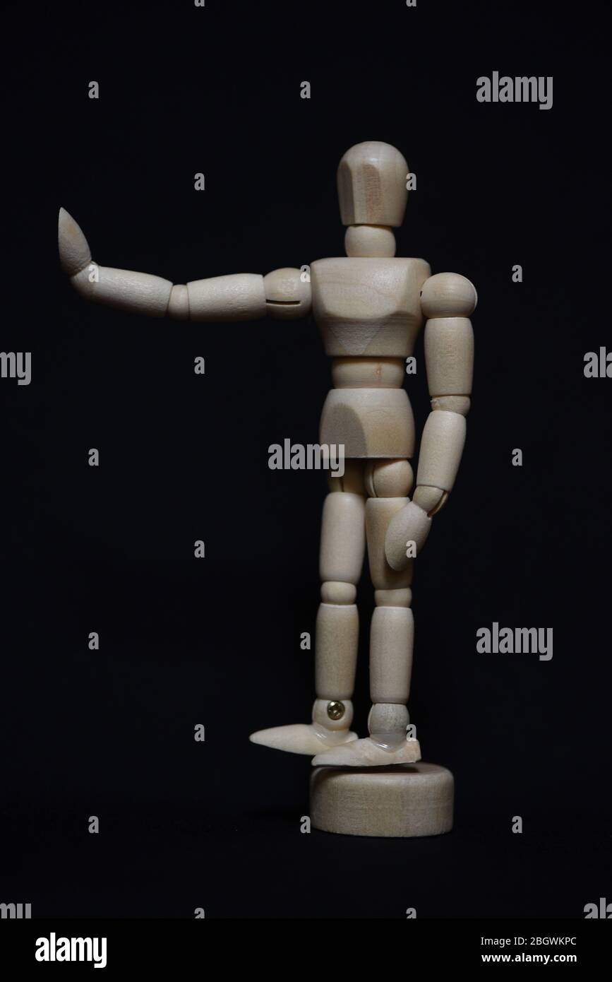 Vertical still life with a wooden articulated artist's manikin or mannequin holding a hand up indicating stop against a black background. Stock Photo