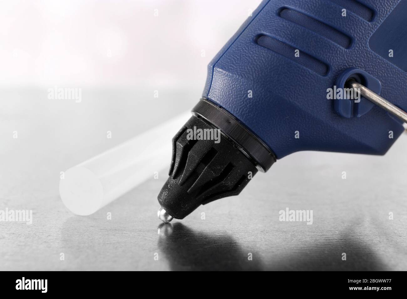 Dark blue glue gun and silicone stick on light background Stock Photo