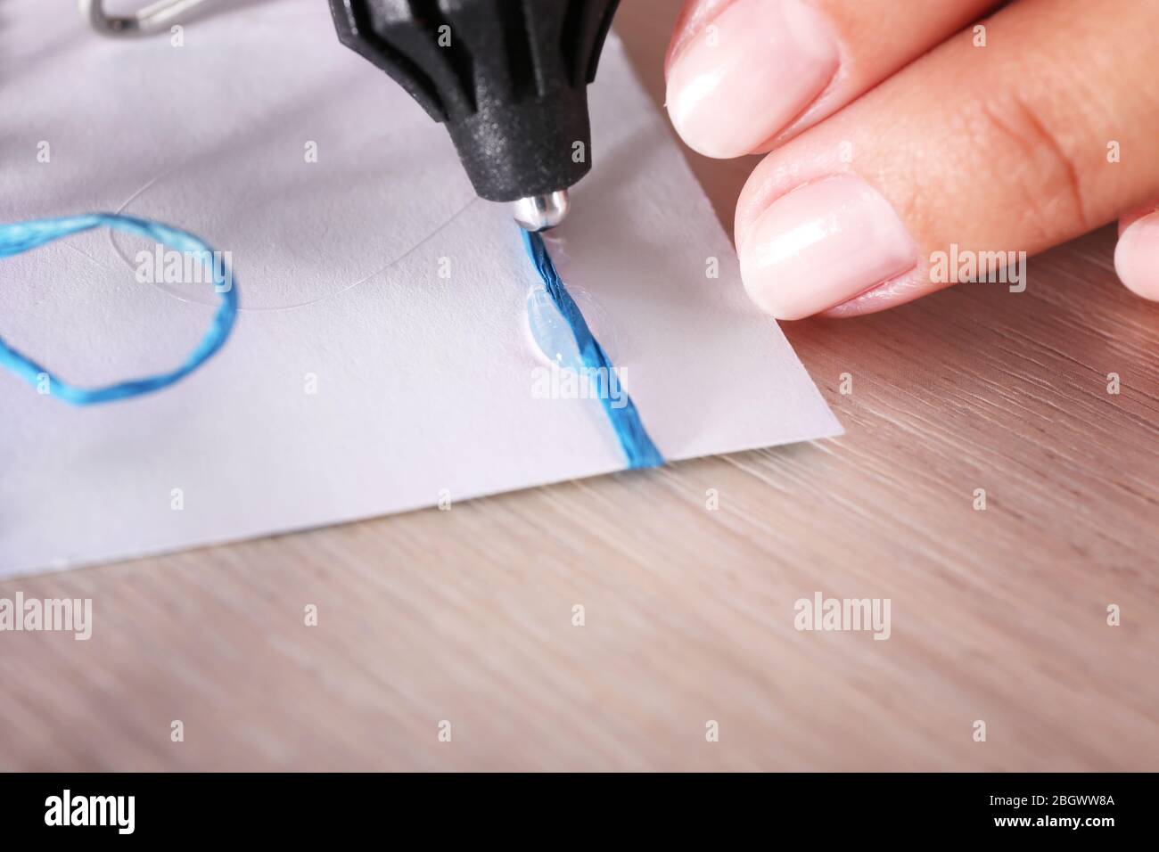 Woman's hand making postcard with blue ribbon and bow with a help of glue gun Stock Photo
