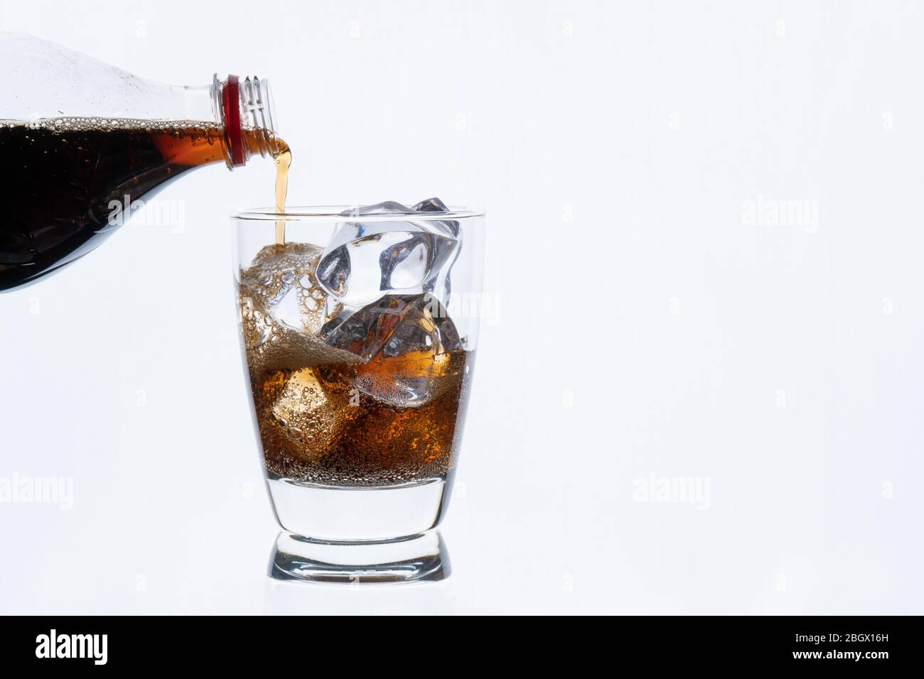 Cold drinking, pouring soda from bottle, glass of cola with ice for hot and summer drink isolated on white background Stock Photo