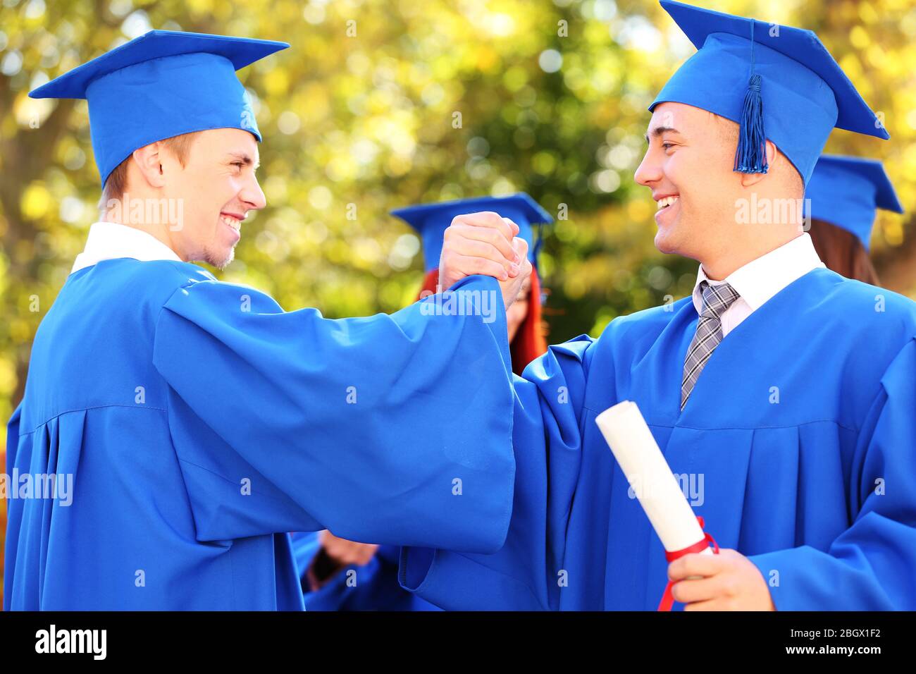 Graduate students wearing graduation hat and gown, outdoors Stock Photo