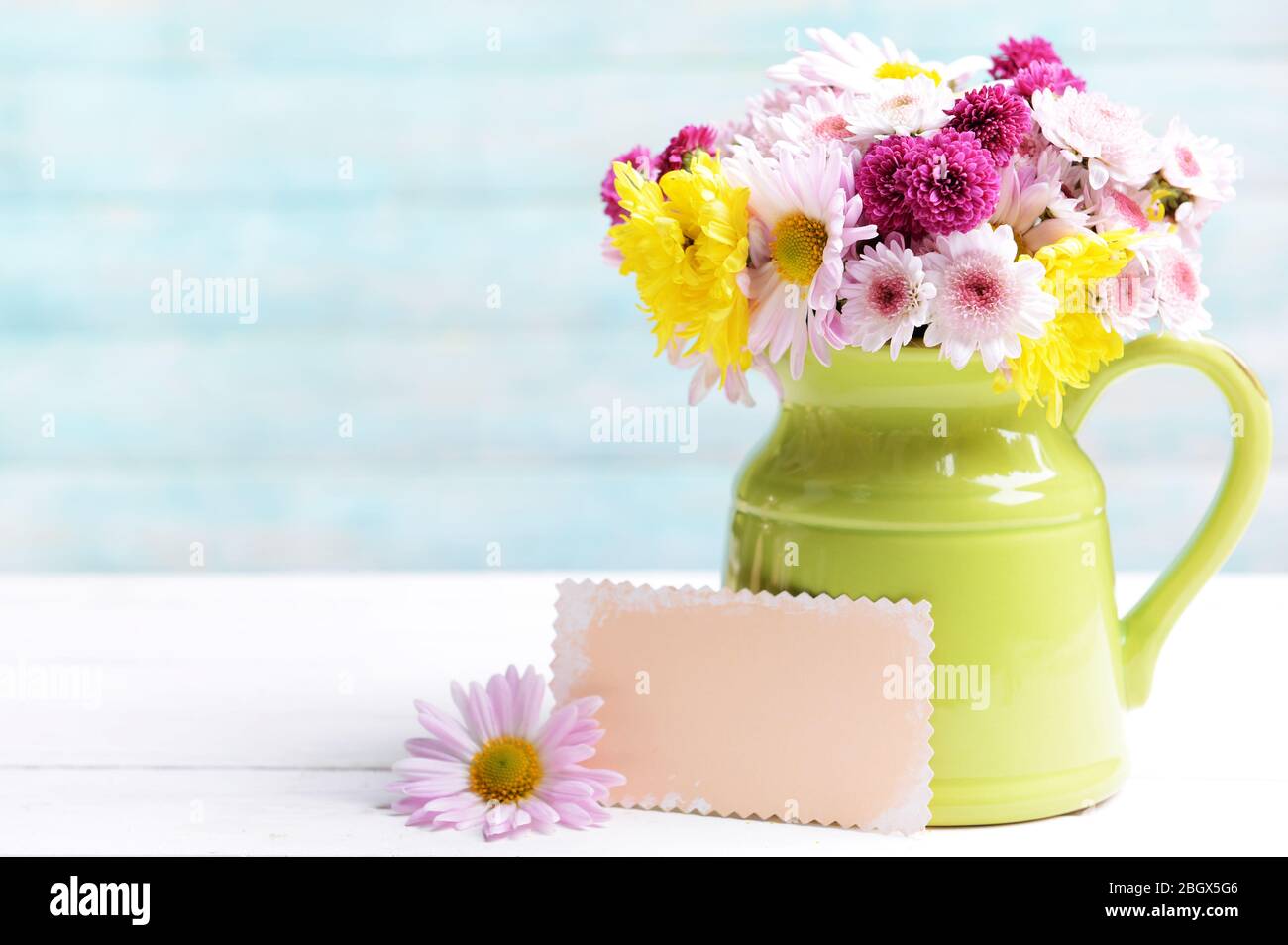 Beautiful flowers in pitcher on table on light blue background Stock