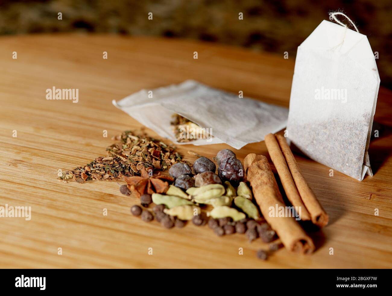 Close up of an open herbal tea bag with loose herbs and juniper berries, cinnamon sticks, allspice, star anise and cardamon on a bamboo cutting board Stock Photo