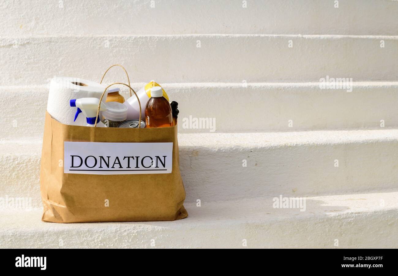 A donation bag filled with food and cleaning supplies on white steps while out for delivery during the Coronavirus / Covid 19 Pandemic Stock Photo