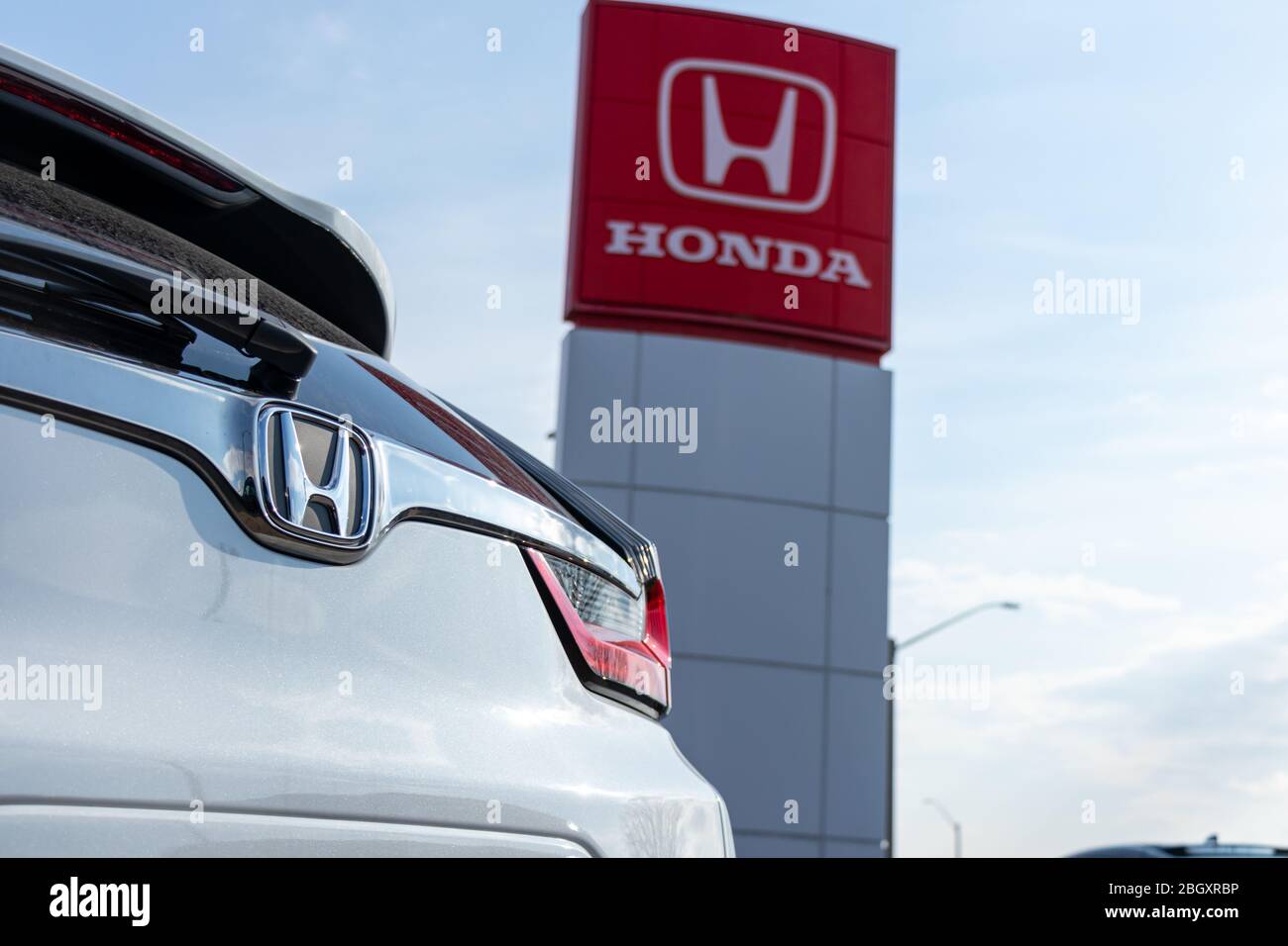 Honda emblem on a car at a dealership, with the Honda Motor Company logo on a sign in the background. Stock Photo