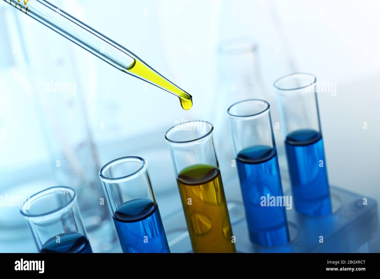 Pipette adding yellow fluid to one of several testtubes with flasks on