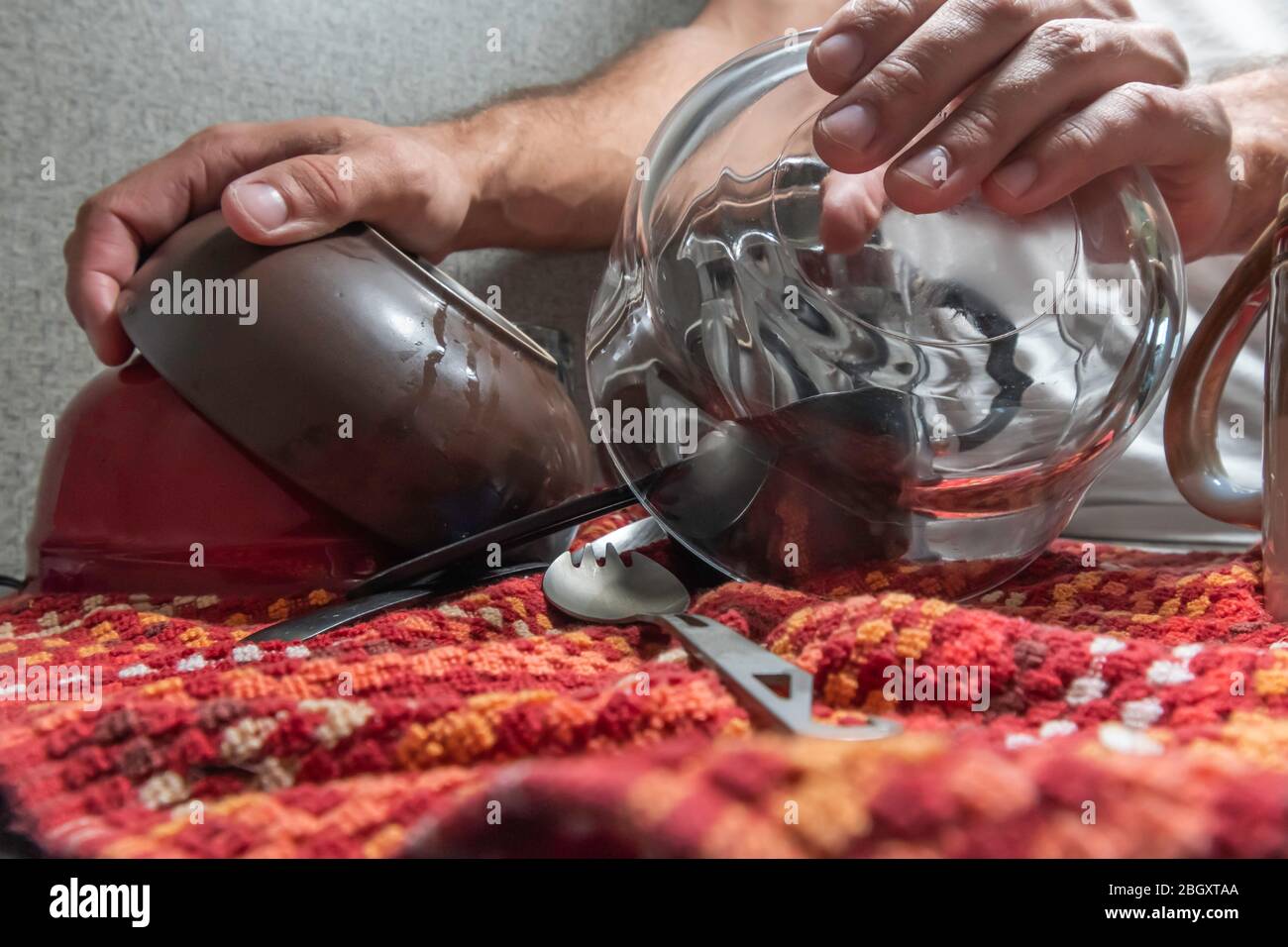 Close up of a person's hands putting away a pile of dishes almost dried away into their storage areas inside. Stock Photo