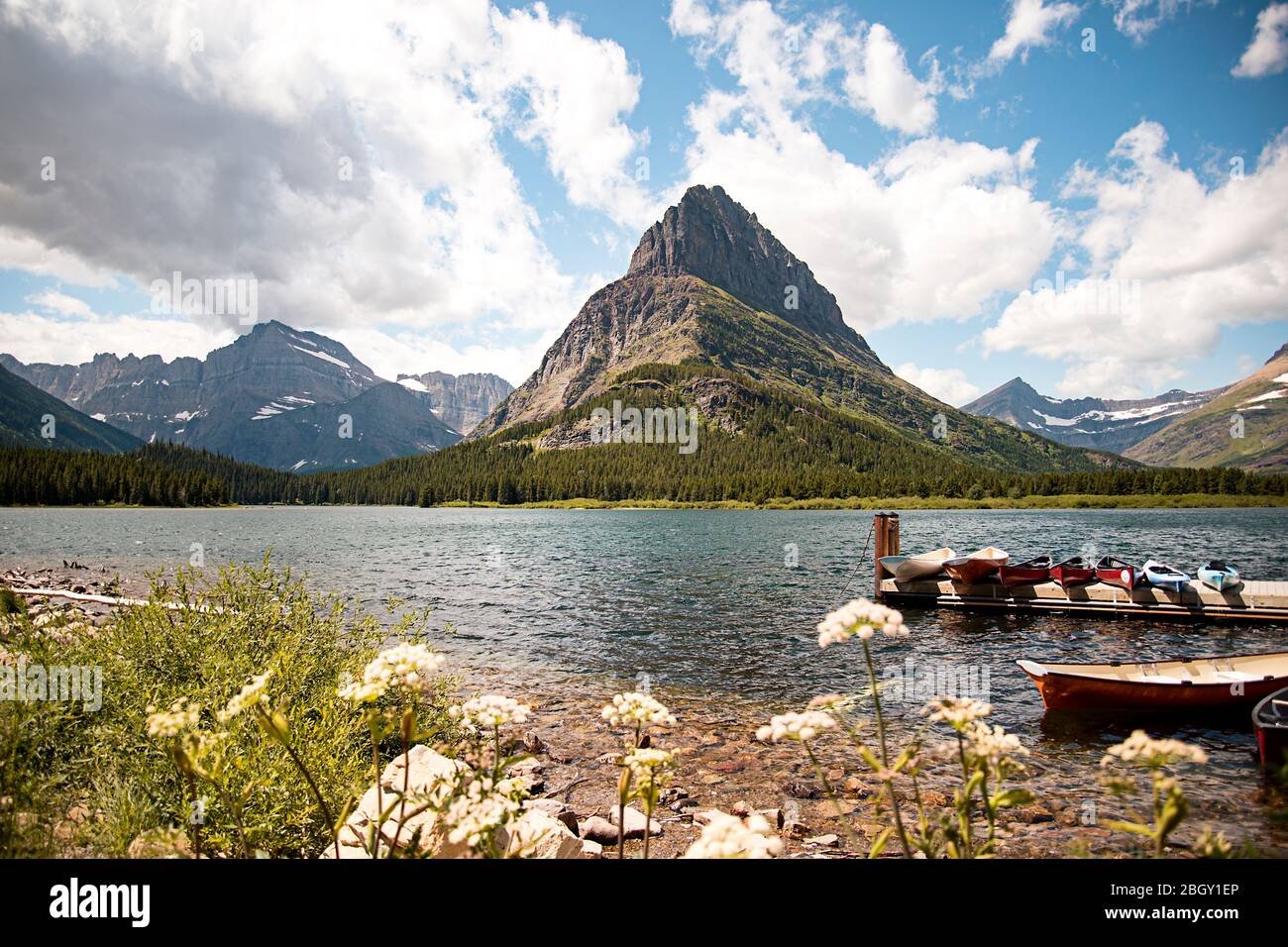Mountain Peak Landscape Scene of Grinnell Point and Swiftcurrent Lake in Glacier National park. Boats docked in the water with a vibrant blue sky abov Stock Photo