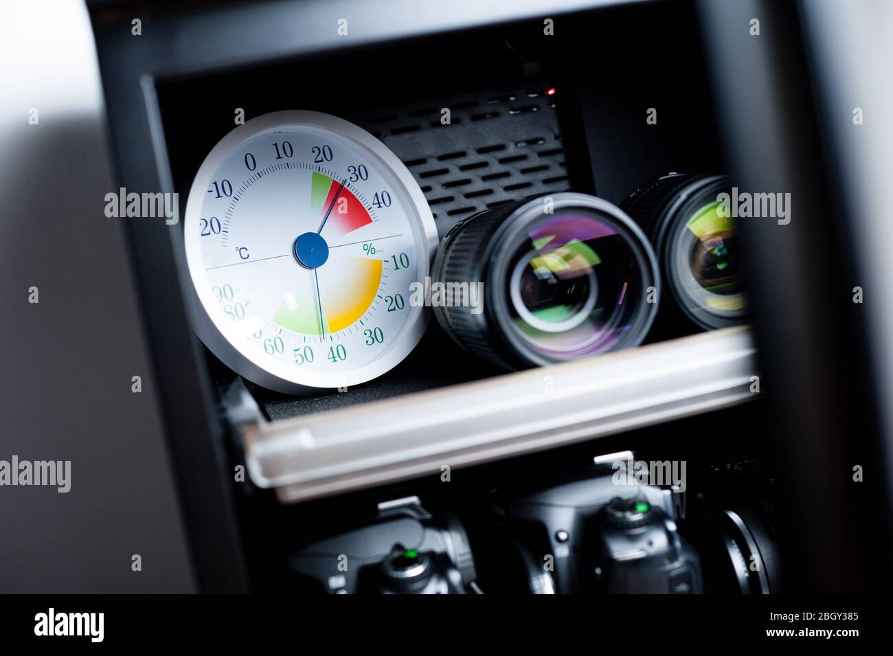 white analog Thermometer and Hygrometer with photography equipments. Lenses and camera equipment are optimally stored at a relative humidity (RH) of a Stock Photo