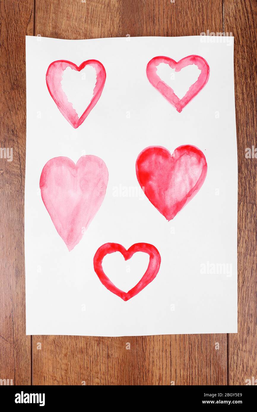 Painted hearts on sheet of paper on wooden table background Stock Photo ...