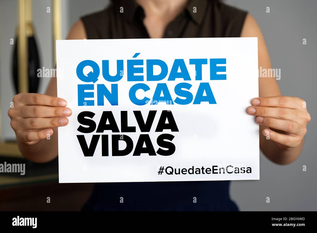 Woman holding sign 'Stay Home Save Lives' in Spanish, global message amid coronavirus crisis. Quarantine message across the globe to fight COVID-19 Stock Photo