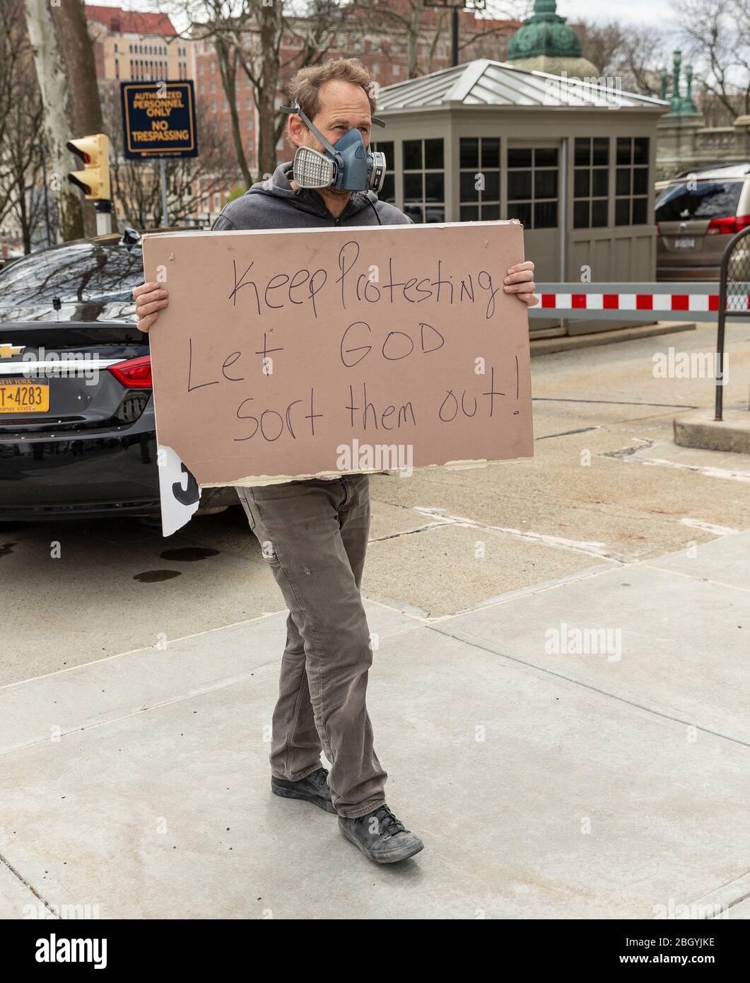 Albany, United States. 22nd Apr, 2020. A man wearing respirator mask holds poster and