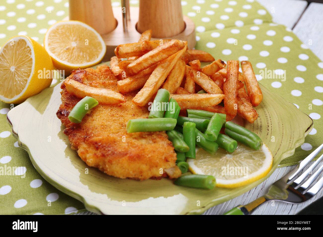 Breaded fried fish fillets and potatoes with asparagus and sliced lemon on plate and wooden planks background Stock Photo