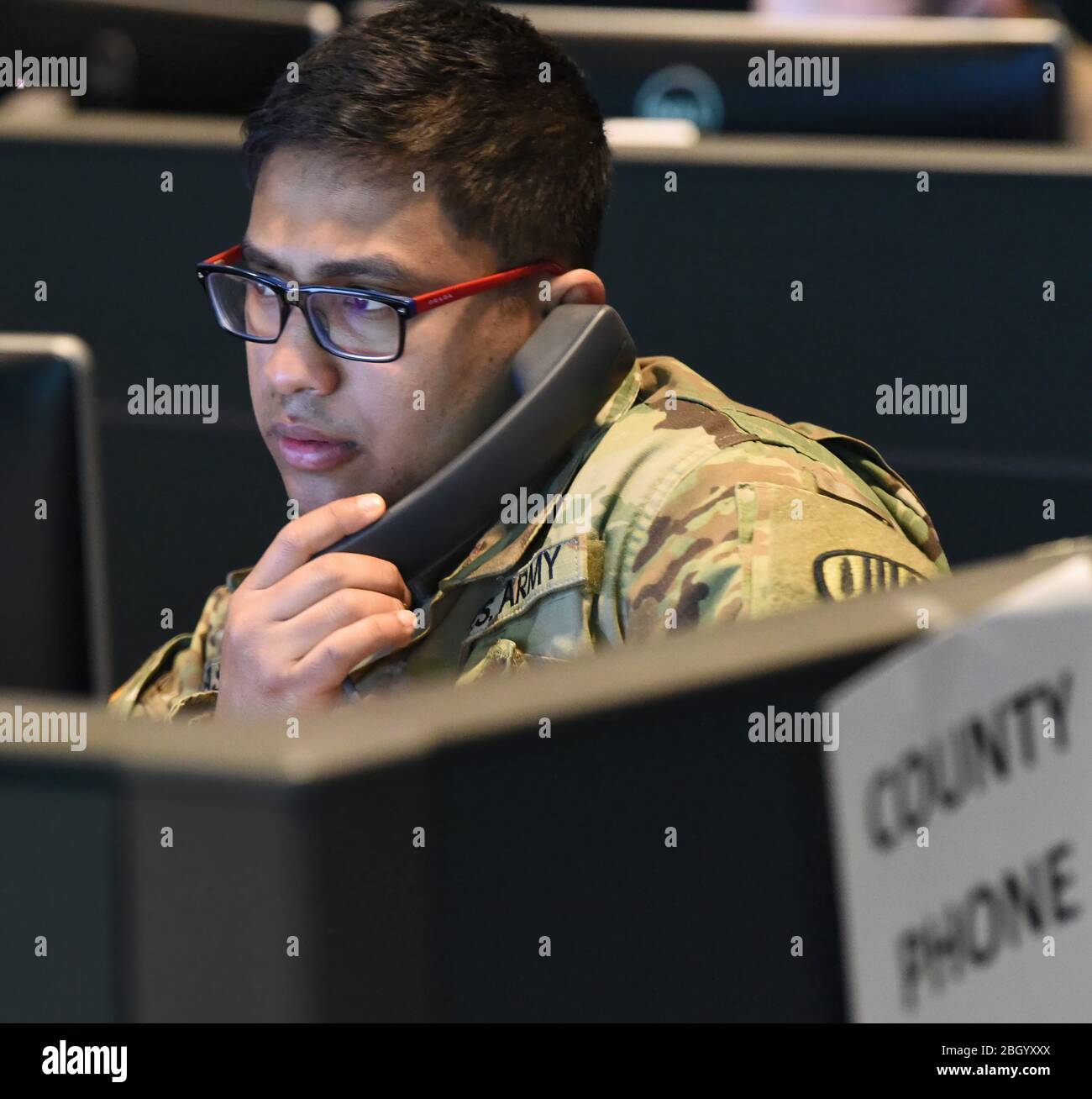 Spc. Jasim Pasha, with the New York Army National Guard 101st Signal Battalion, speaks to someone who has called the Coronavirus Hotline in Hawthorne, N.Y., March 16, 2020. The New York State Department of Health established a toll-free Coronavirus Hotline (1-888-364-3065). (U.S. Air National Guard photo by Senior Airman Sean Madden) Stock Photo