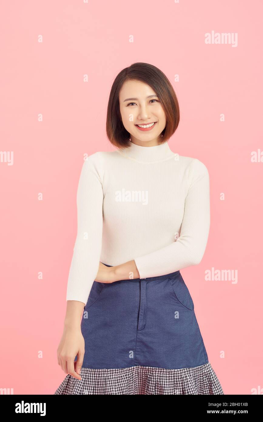 Portrait of smiling Asian woman standing isolated on pink background. Stock Photo