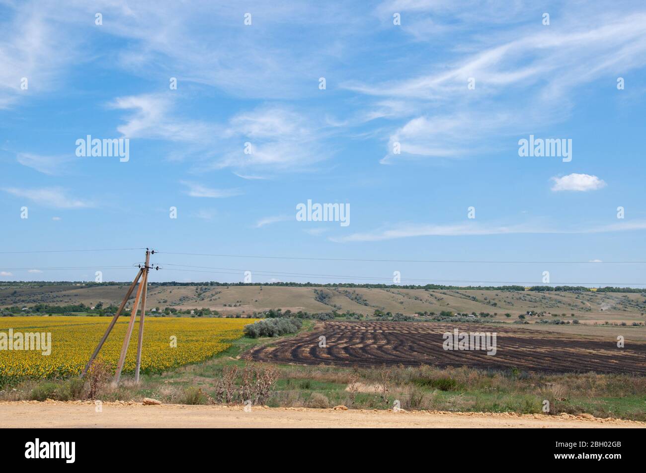 Old electric pillar near country road along agricultural fields. Rural landscape of fields and clear blue sky with white spindrift clouds. Summer idyl Stock Photo