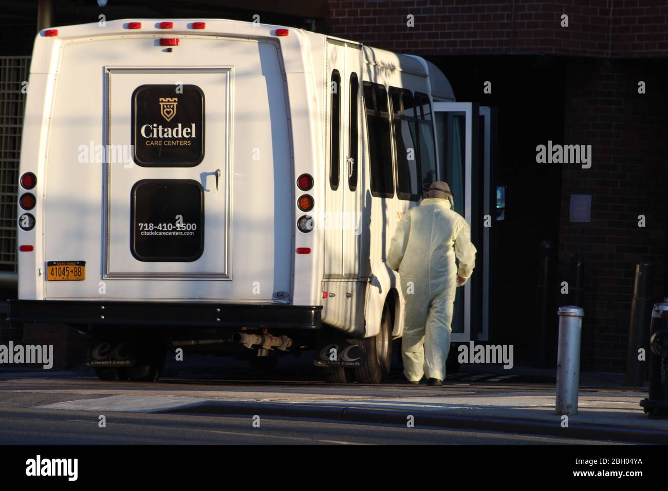 New York, New York, USA. 22nd Apr, 2020. This man dressed in a yellow hazmat heads to a rehab and nursing center skirting an elderly transport bus in the Bronx, New York City. 3425 residents of New York state nursing homes including 554 in Bronx have died so far because of COVID-19. That represents nearly 25% of the state's pandemic deaths. Credit: Marie Le Ble/ZUMA Wire/Alamy Live News Stock Photo
