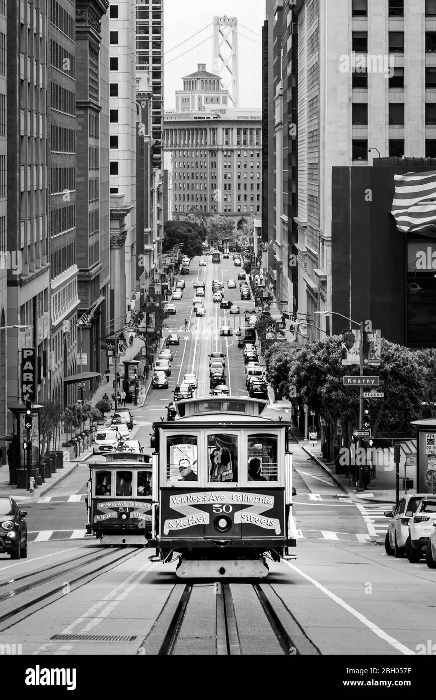 A traditional cablecar is running downtown on a sloping street; in the distance, the Bay Bridge Stock Photo