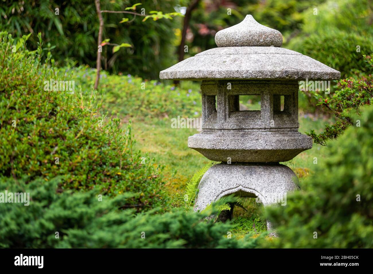 Close up of a stone japanese votive lantern, surrounded by green bushes and hedges at the Japanese Tea Garden in San Francisco Stock Photo