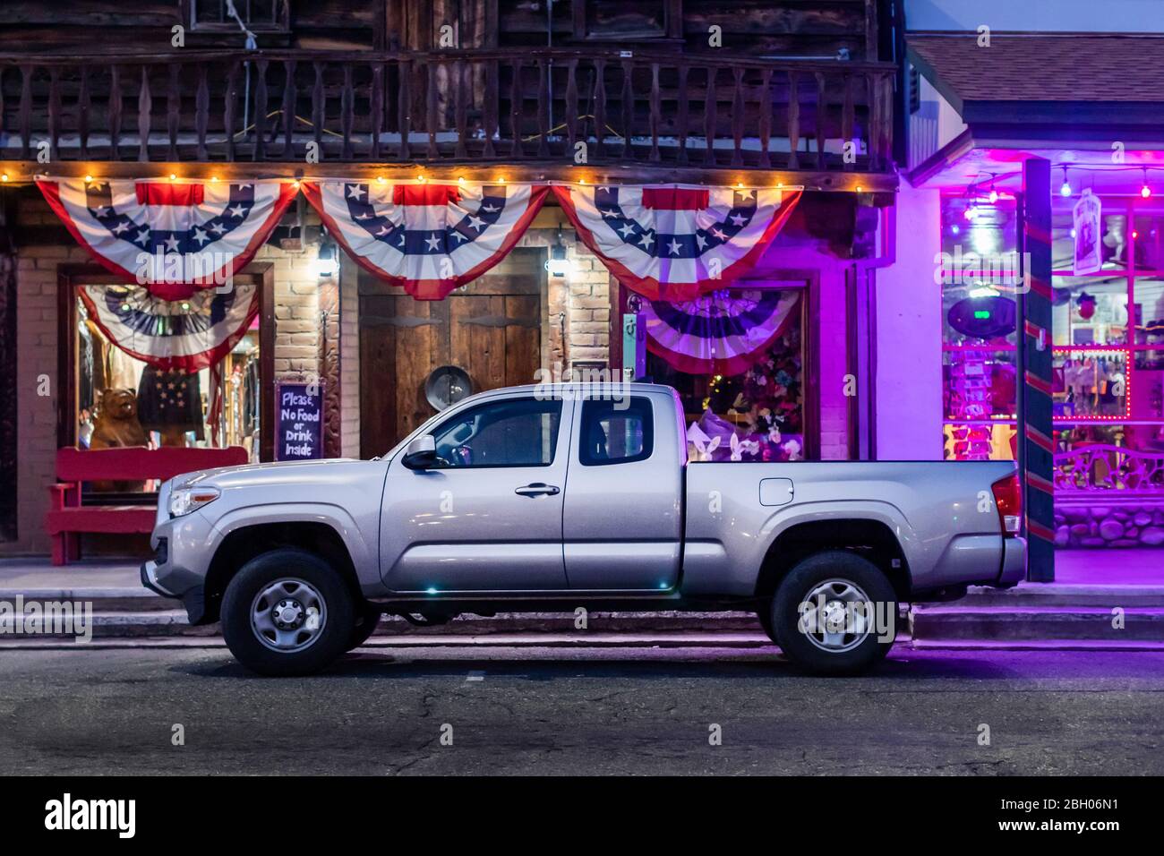 Close up nightshot of a grey pickup truck parked in front of a roadside shop decorated with patriotic ribbons and flags Stock Photo
