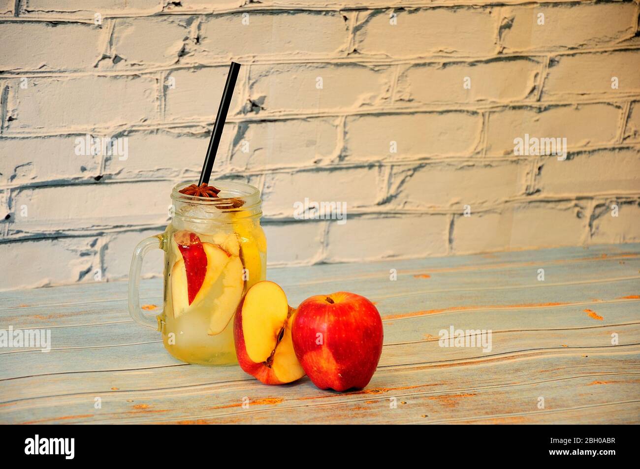 A glass mug of apple juice with ice and two red apples stand on a wooden table. Close-up. Stock Photo