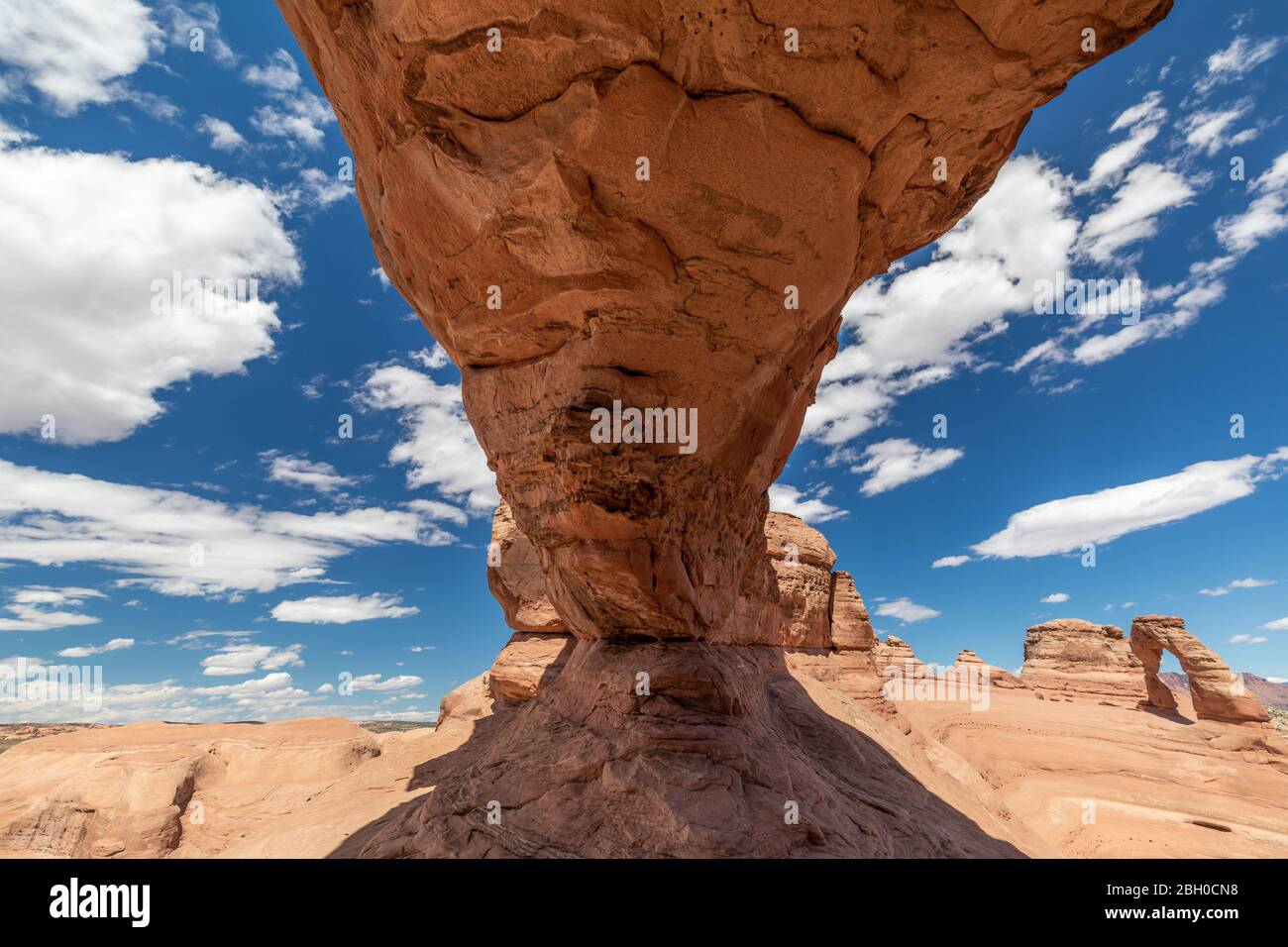 A blue sky with puffy clouds is divided by a stone arch; in the distance the Delicate Arch can be seen Stock Photo