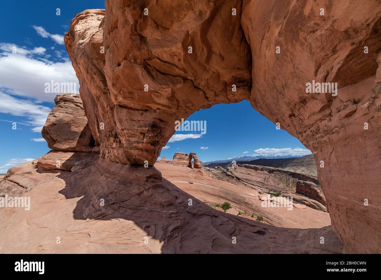 The stone arch known ad Delicate Arch as seen through a nearby arch, against a blue sky with puffy clouds Stock Photo