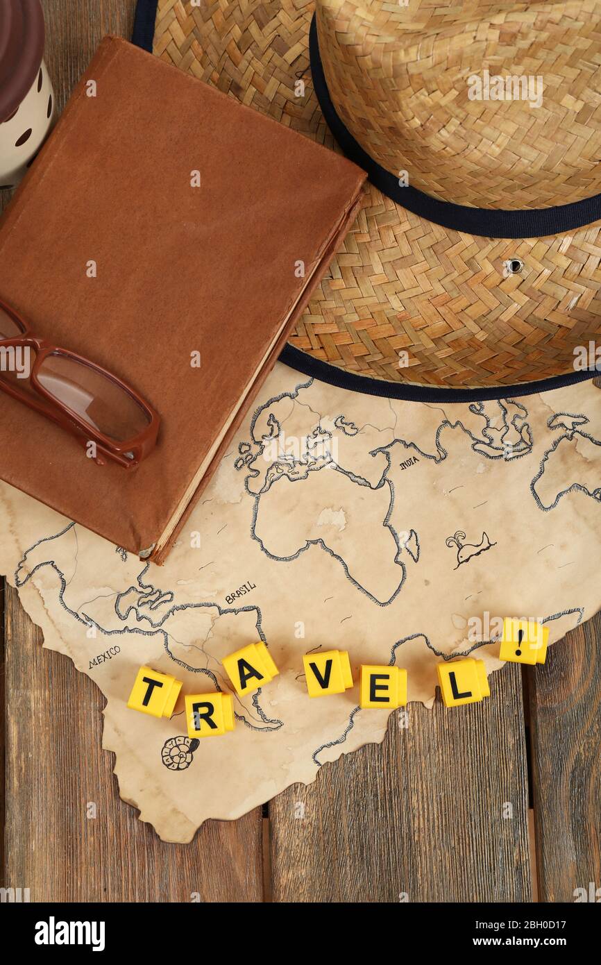 Straw hat, book and glasses with word Travel on world map and wooden planks background Stock Photo