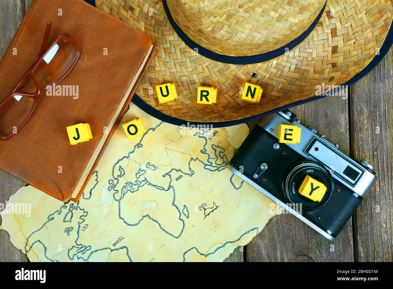 Straw hat, book, camera and glasses with word Journey on world map and wooden planks background Stock Photo