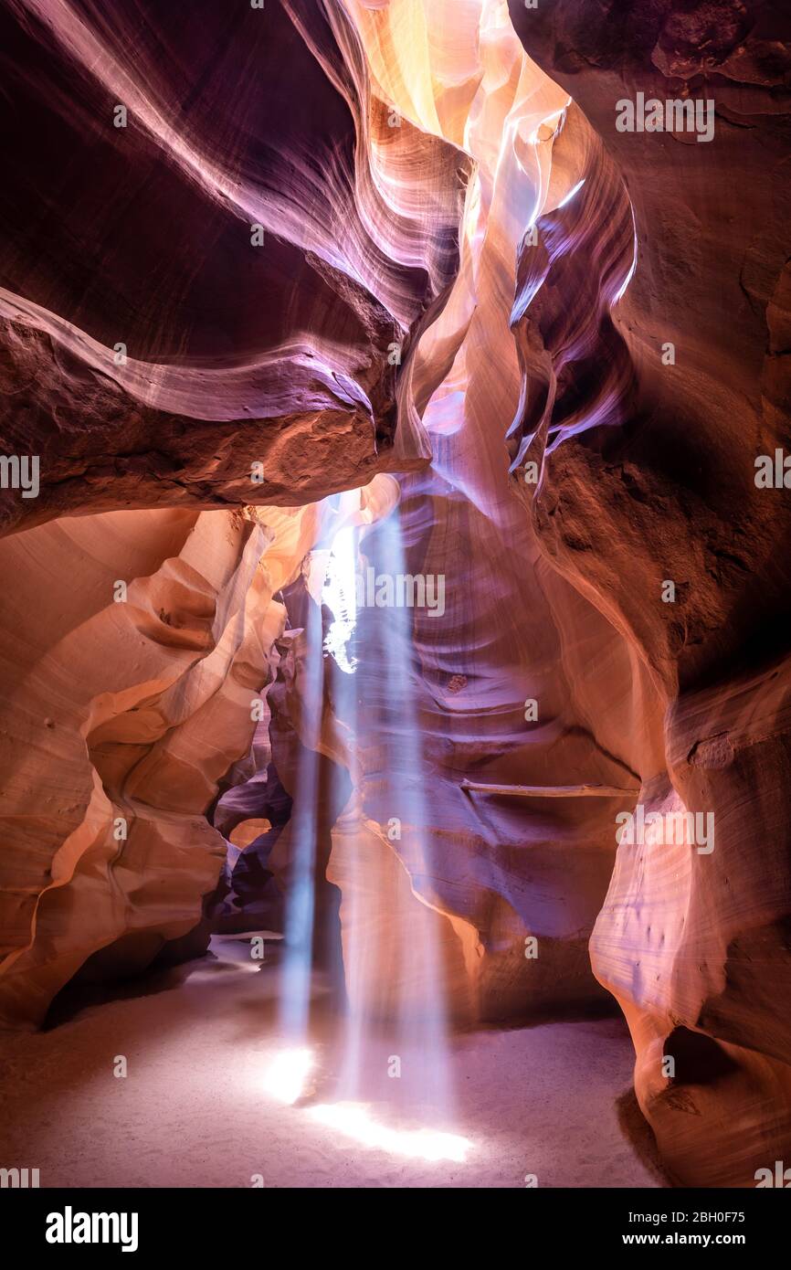 In the Upper Antelope Canyon, three beams of sun light shine through an opening in the vault and down on the sandy floor Stock Photo