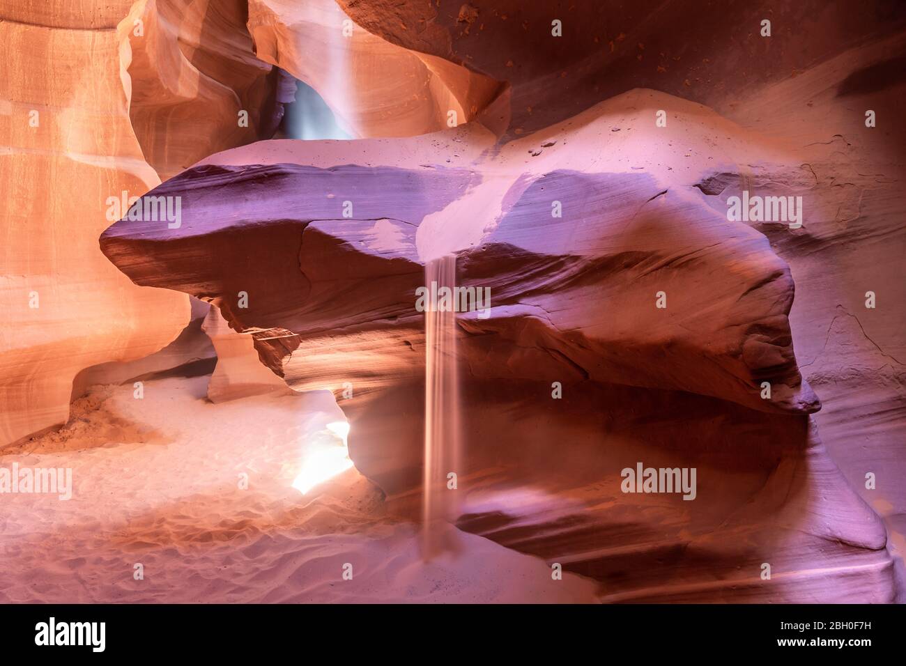 Close up shot of a red sandstone rock in Antelope Canyon, with sand flowing and a beam of sunlight falling from an opening in the the vault Stock Photo
